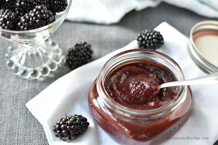 jar of blackberry barbecue sauce with bowl of blackberries behind. 