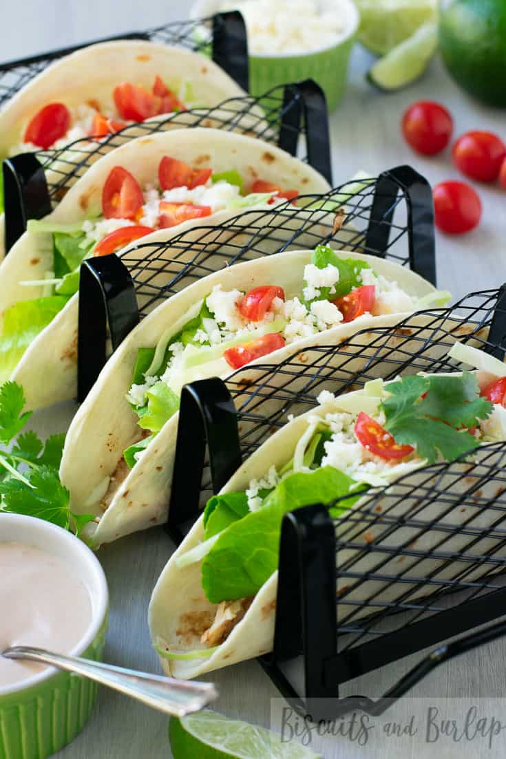 grilled fish tacos in a stand with sauce on side.
