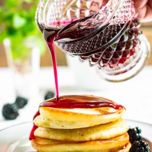 blackberry syrup being poured on pancakes.
