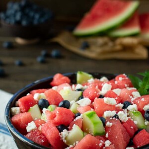 watermelon salad in bowl with watermelon & blueberries behind