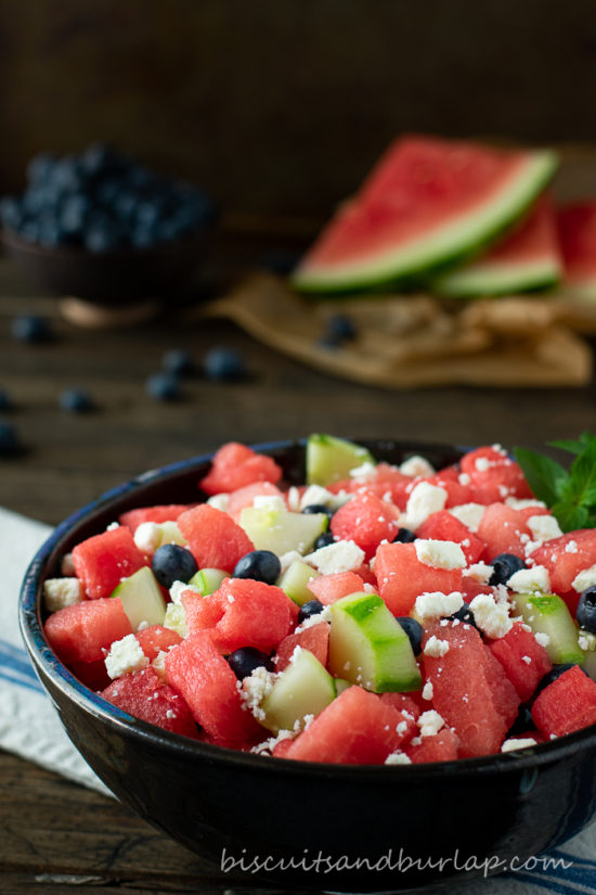 watermelon salad in bowl with watermelon & blueberries behind