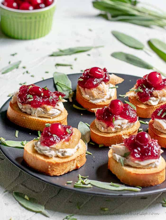 Turkey appetizers topped with cranberry sauce on a black plate sprinkled with fresh sage