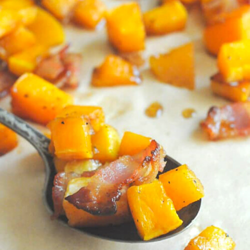 A spoon filled with bacon butternut squash lying on a baking sheet.