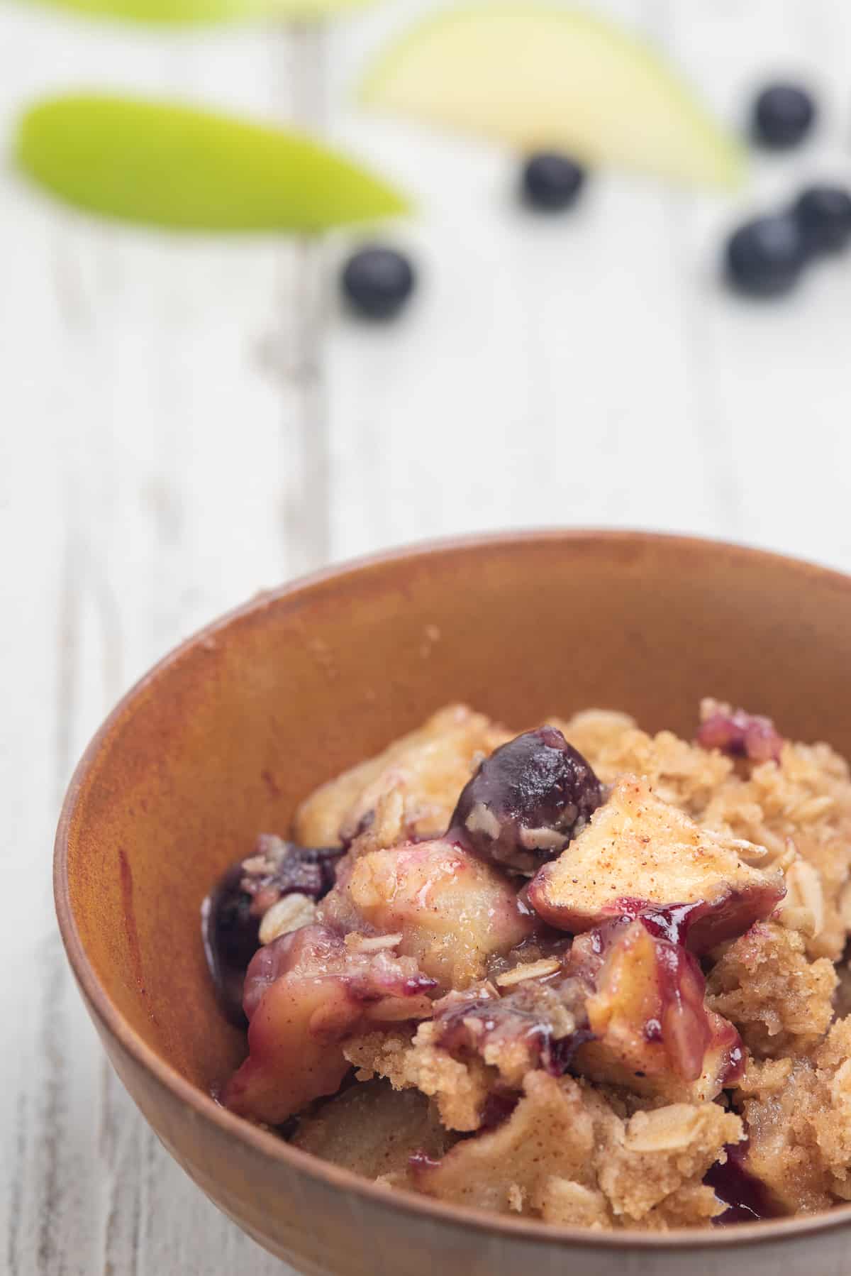 apple blueberry crisp in a brown bowl on a white background