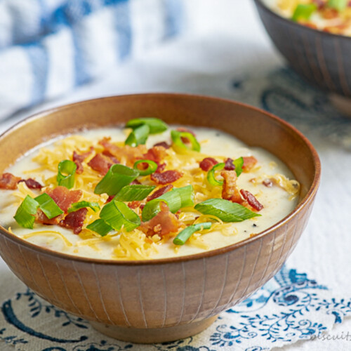 A brown bowl of easy potato soup topped with sliced green onions, crumbled bacon, and cheddar cheese.