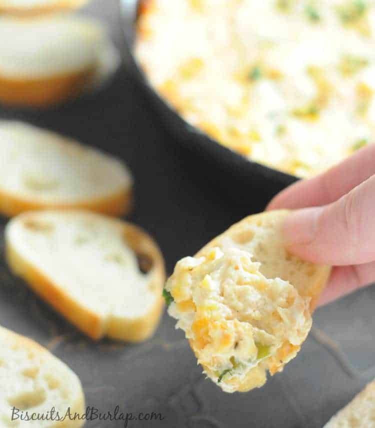 and hand holding a piece of French bread that has been dipped in crab dip.
