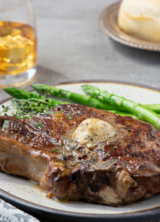 steak with butter on top and bread and whisky behind