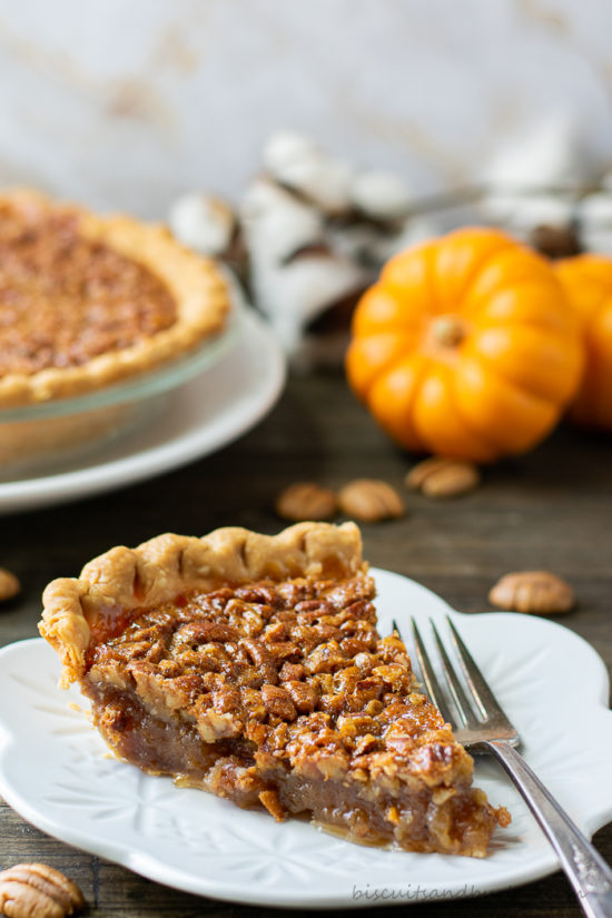 slice of pecan pie with whole pie and small pumpkin behind