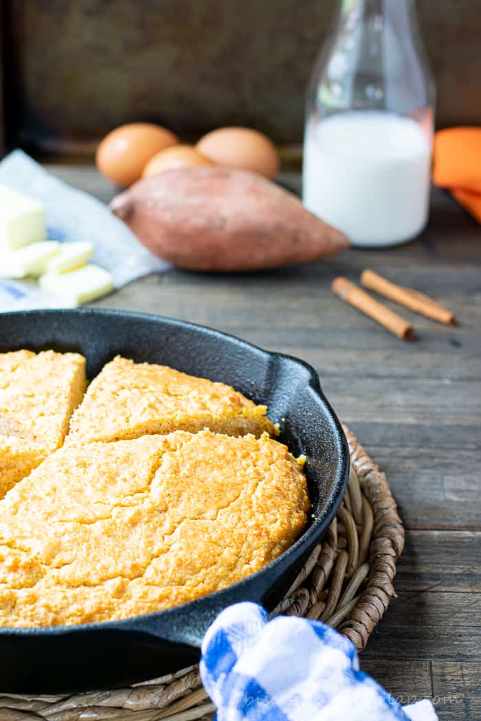 vertical shot of sweet potato cornbread in skillet with eggs and buttermilk behind