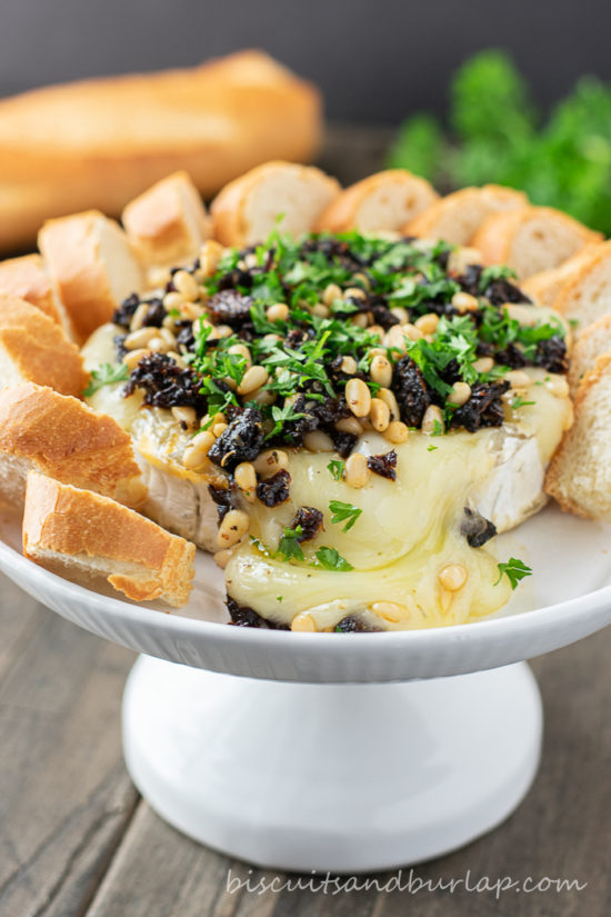baked brie cheese on stand surrounded by crostini