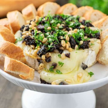 baked brie cheese on stand surrounded by crostini