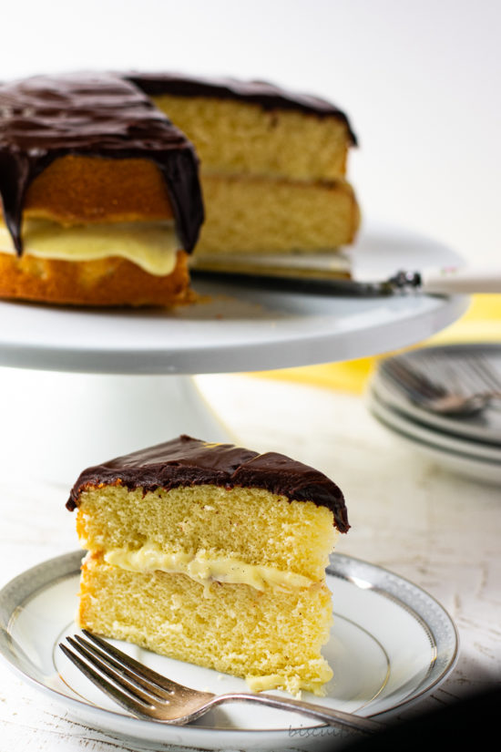 slice of boston cream pie on plate with fork and cake in background