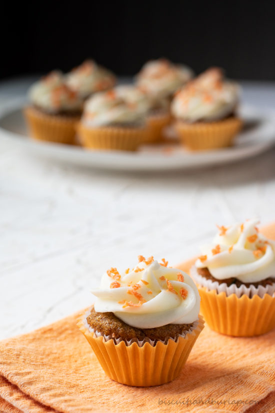 one carrot cupcake on orange cloth with more behind