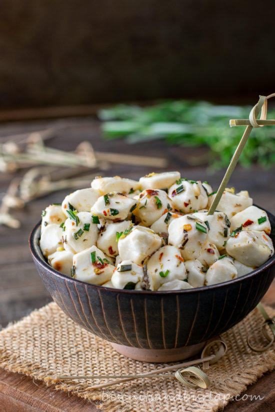 vertical shot of bowl of mozzarella pearls with herbs behind