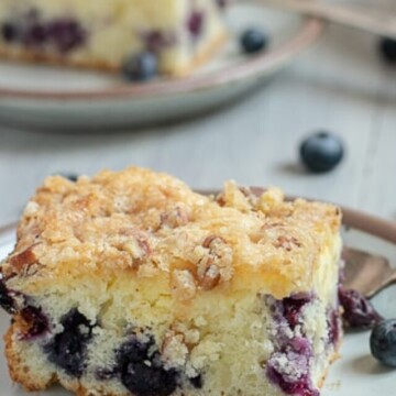 one slice of blueberry crumb cake on plate with another behind