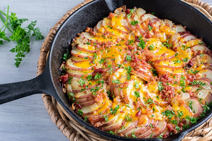 potatoes in a cast iron skillet topped with cheese, bacon, and fresh herbs.