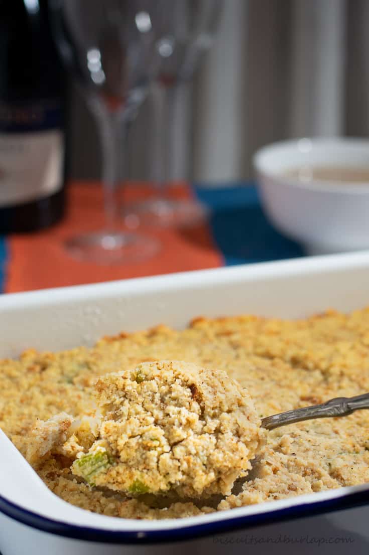 A spoon lifting out a serving of cornbread dressing from a white baking dish. 