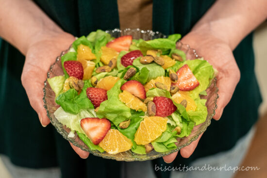 hands holding a salad with tangerines & strawberries