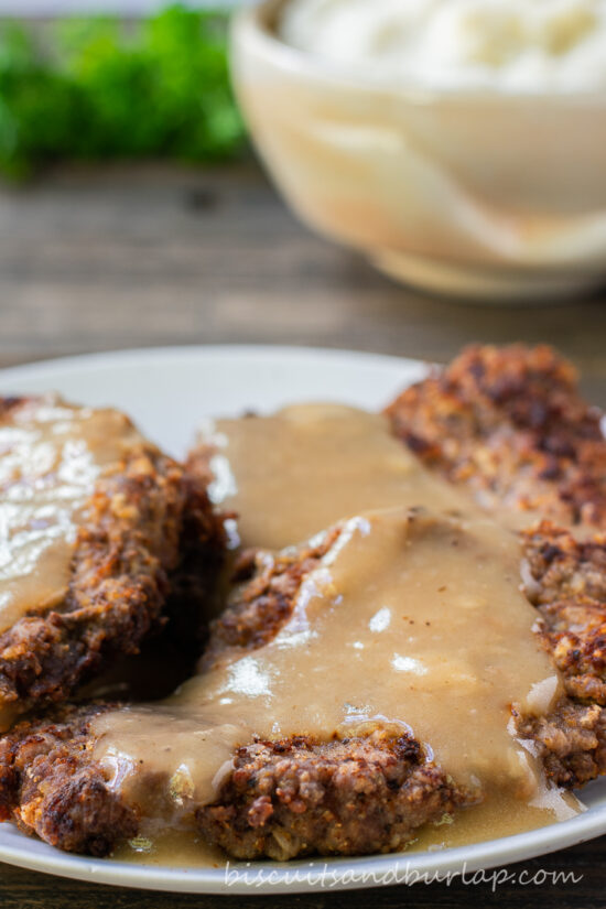 country fried steak on plate with potatoes behind