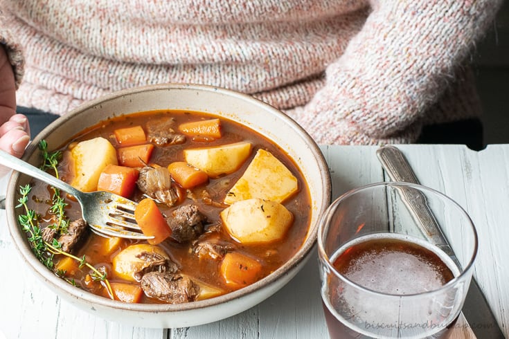 A person eating Guinness Irish stew with a glass of beer in the foreground.