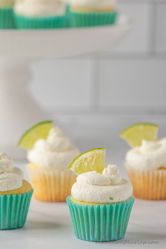 key lime cupcakes on counter and more behind on stand