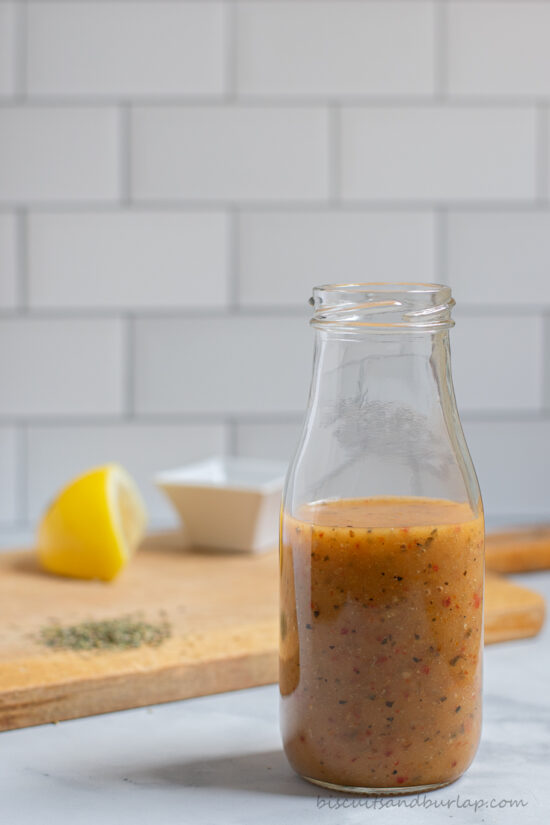 bottle of salad dressing with herbs and lemon on board