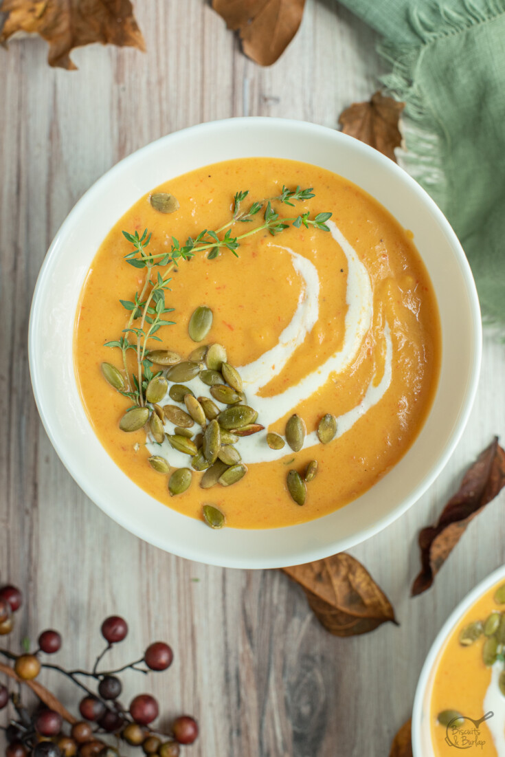 Red Pepper and butternut squash Soup in a white bowl topped with pumpkin seeds and thyme