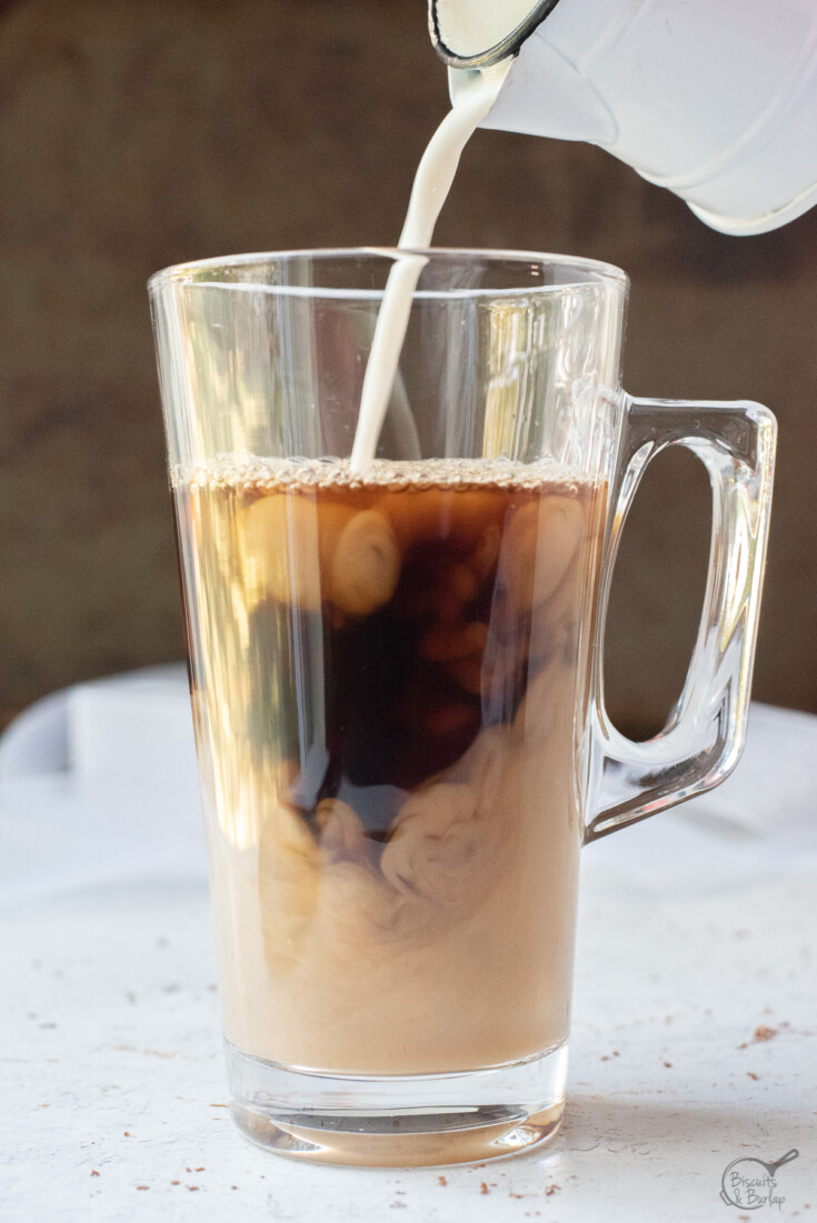 Pouring milk into coffee in a glass mug