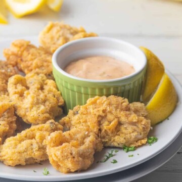Fried oysters and remoulade sauce and lemons on white plate