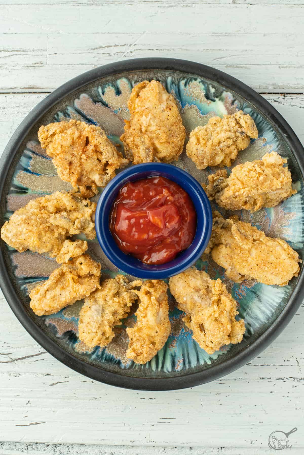 Fried oysters and cocktail sauce in blue bowl.