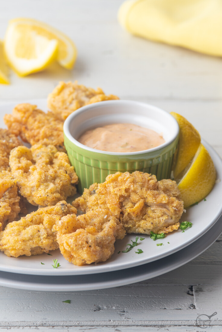 Fried oysters and remoulade sauce and lemons on white plate