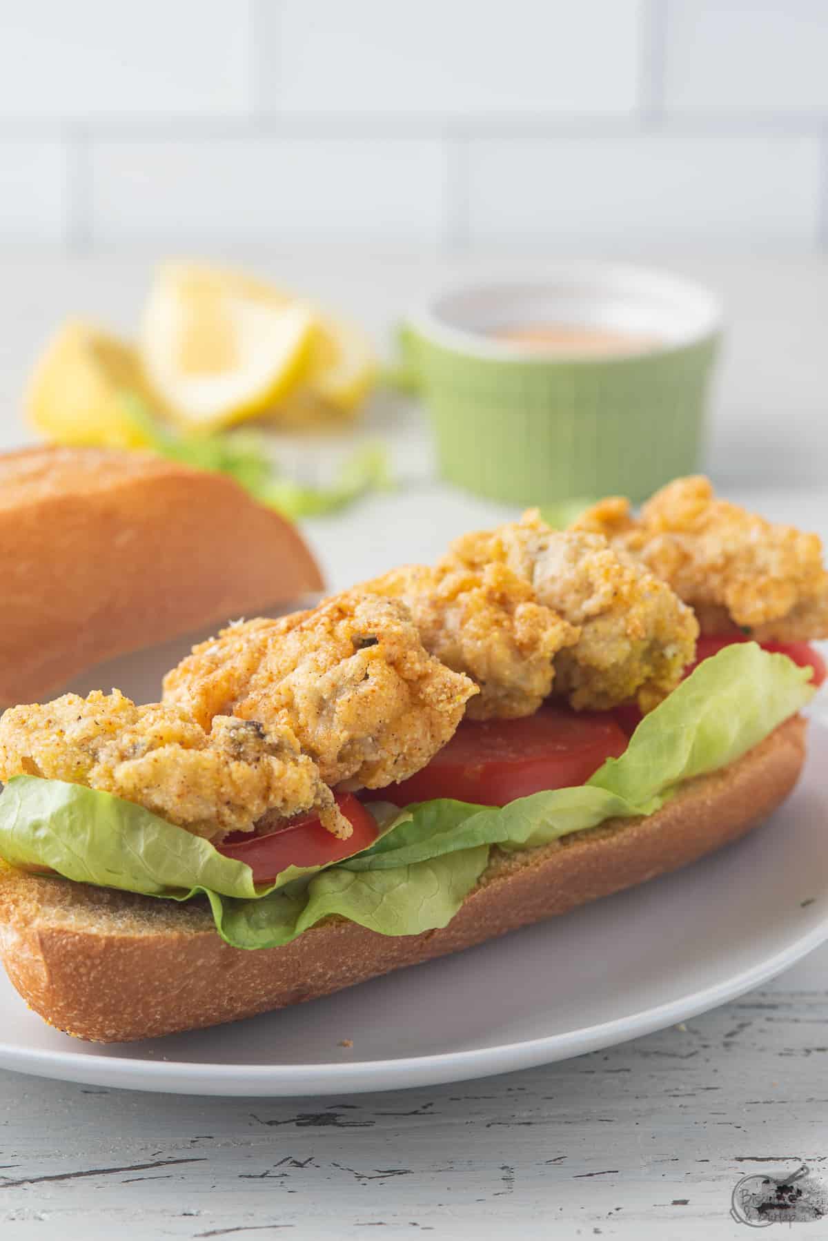 fried oyster poboy on white plate with remoulade in background