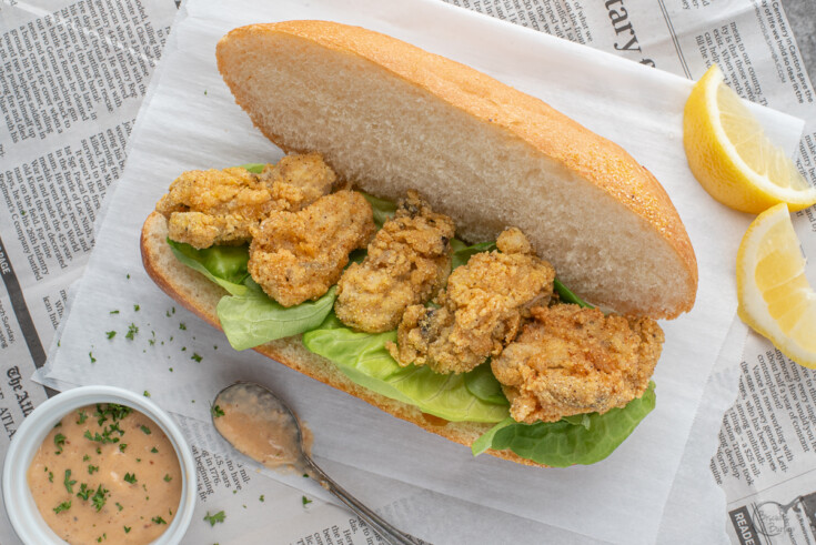 fried oyster po boy on parchment paper and newspaper with remoulade and lemon slices