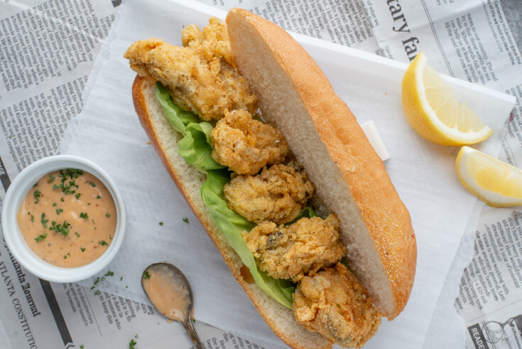 fried oyster po boy on parchment paper and newspaper with remoulade and lemon slices