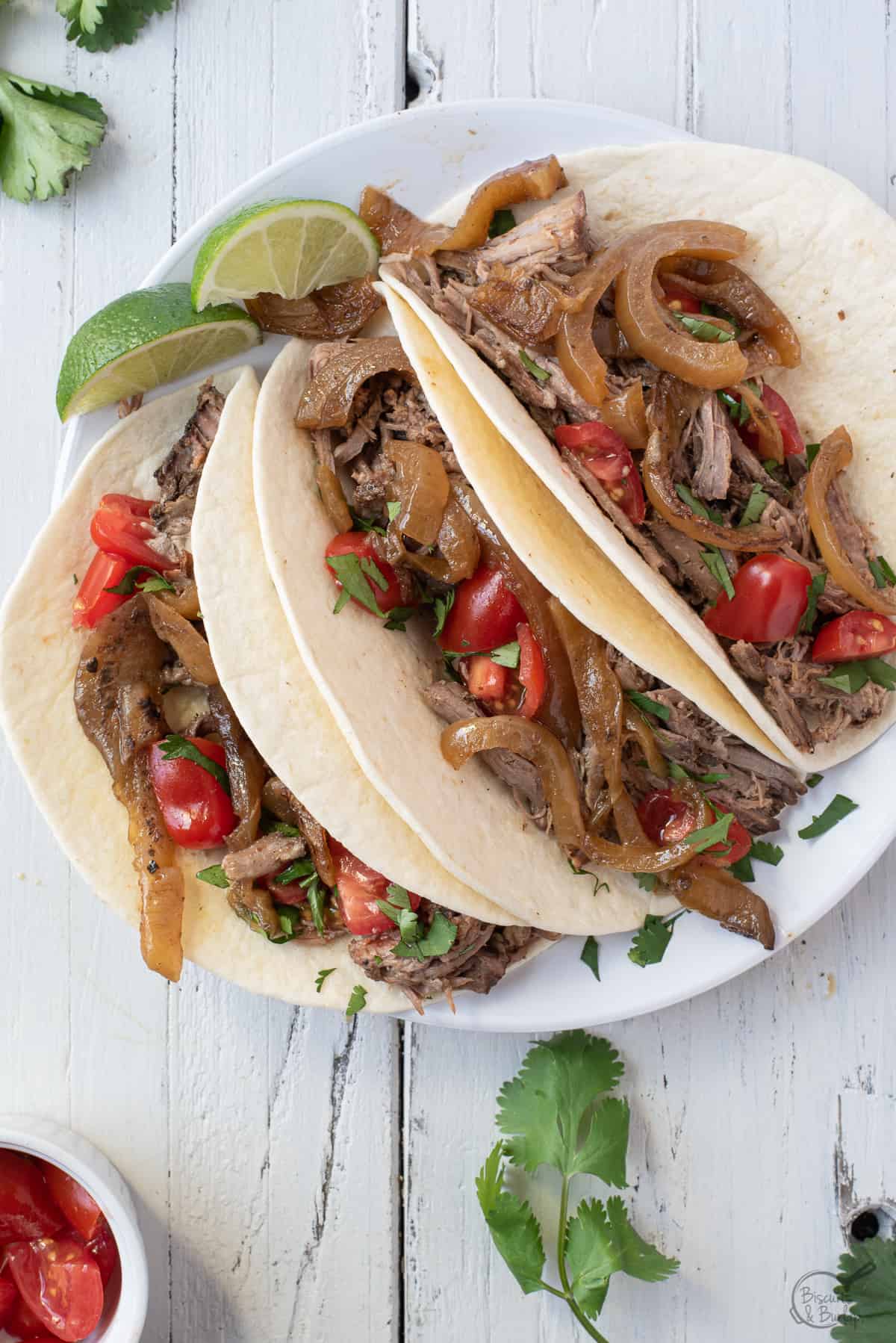 tacos with shredded beef , onions and tomatoes.