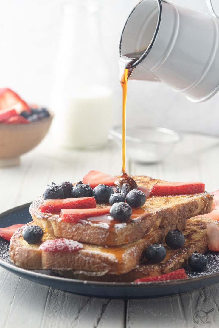 sourdough french toast with syrup being poured and berries on top.