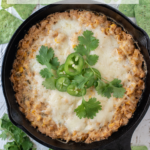 Corn dip with cream cheese in a cast iron skillet with tortilla chips and cilantro