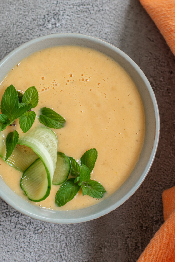 bowl of chilled peach soup with  mint and cucumber on top