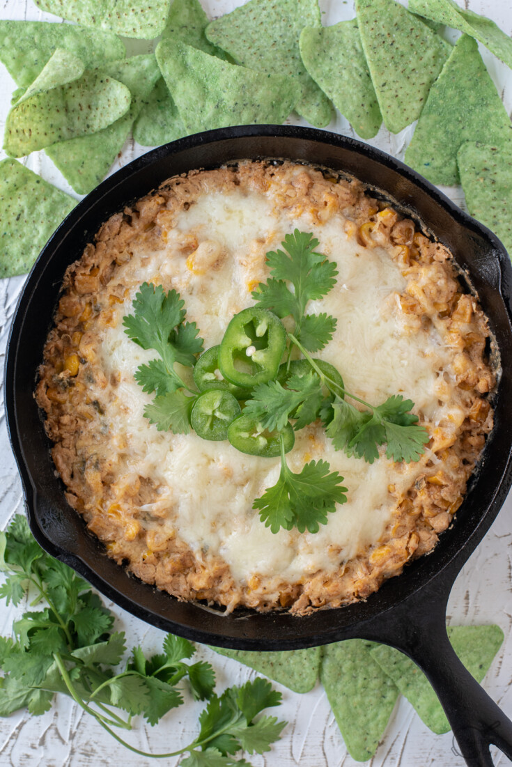 Corn dip with cream cheese in a cast iron skillet with tortilla chips and cilantro