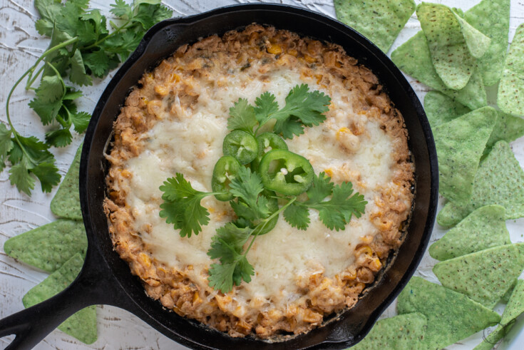 Corn dip with cream cheese in a cast iron skillet with tortilla chips and cilantro