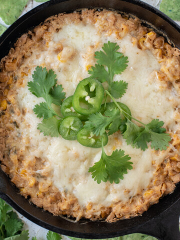 Corn dip with cream cheese in a cast iron skillet with tortilla chips and cilantro