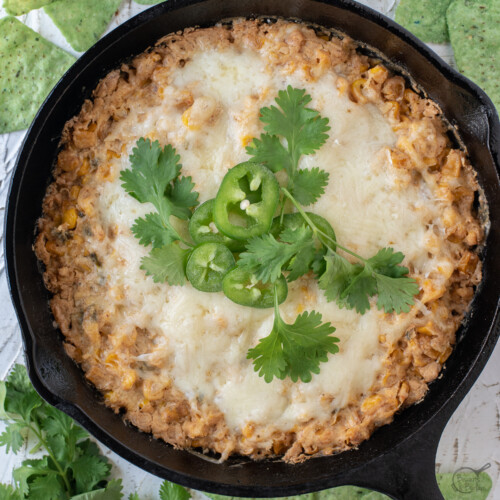 Corn dip with cream cheese in a cast iron skillet with tortilla chips and cilantro