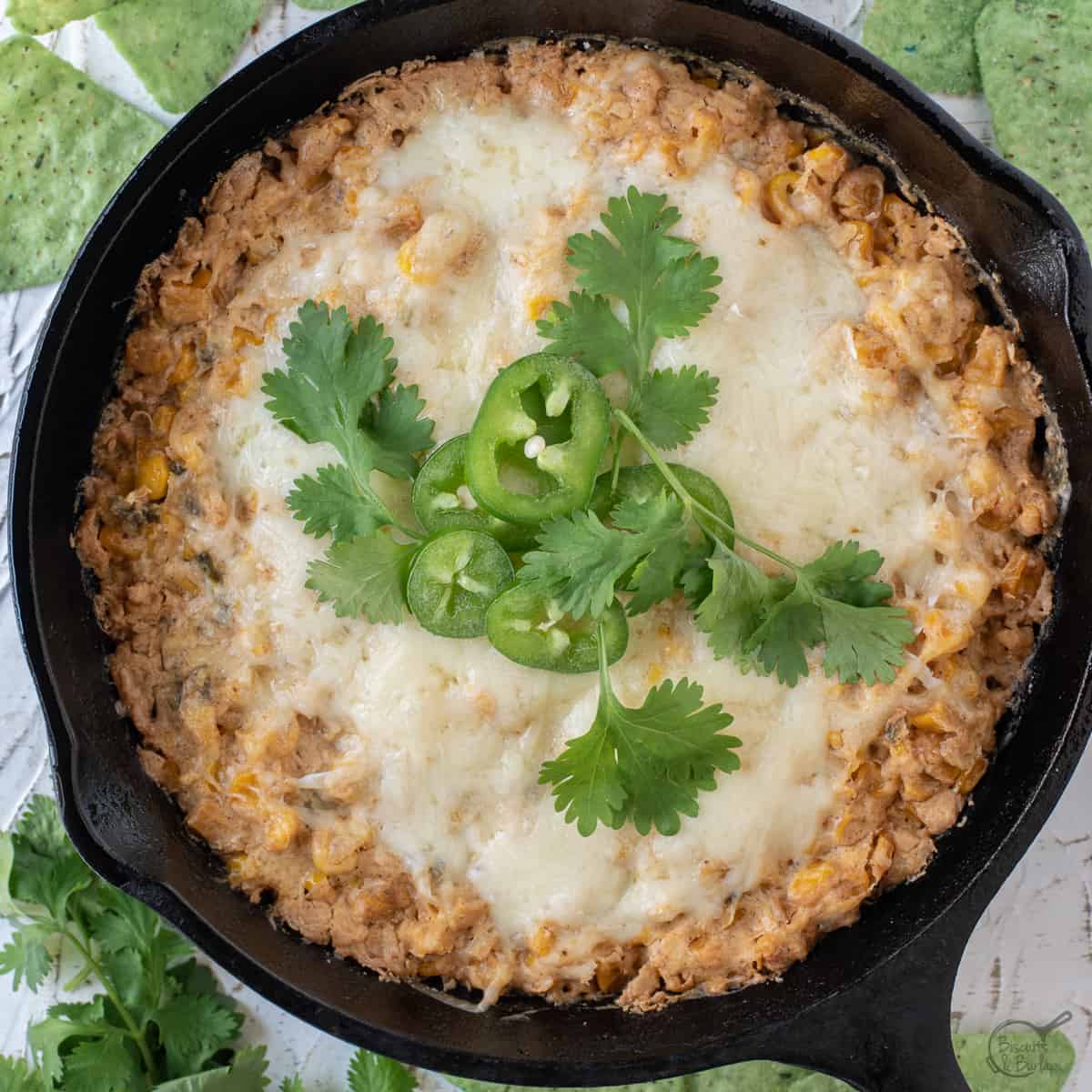 Corn dip with cream cheese in a cast iron skillet with tortilla chips and cilantro