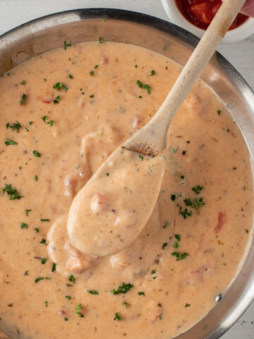 wooden spoon of creole cream sauce over skillet.