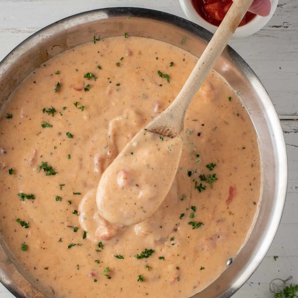 wooden spoon of creole cream sauce over skillet.