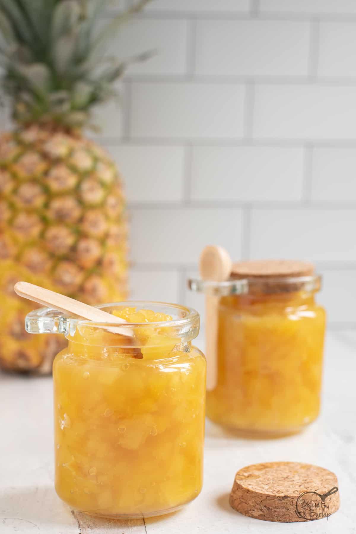 one open jar of pineapple jam with another behind.