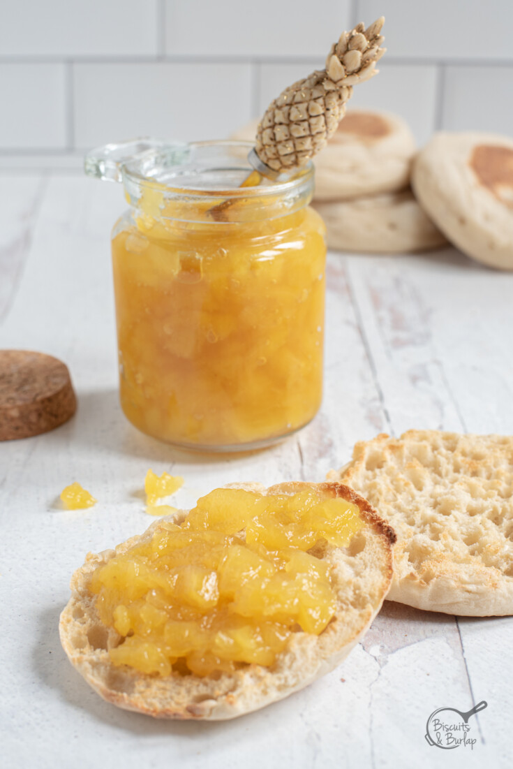 pineapple preserves on English muffin half with jar behind.