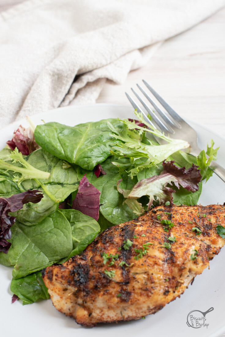 piece of blackened chicken on plate with salad.