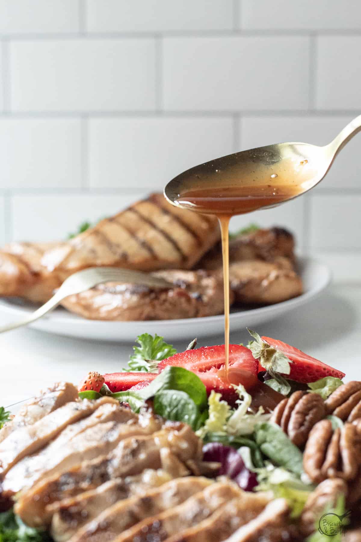 dressing being drizzled over salad with grilled chicken.