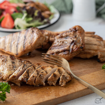 sliced grilled chicken for salad on cutting board.